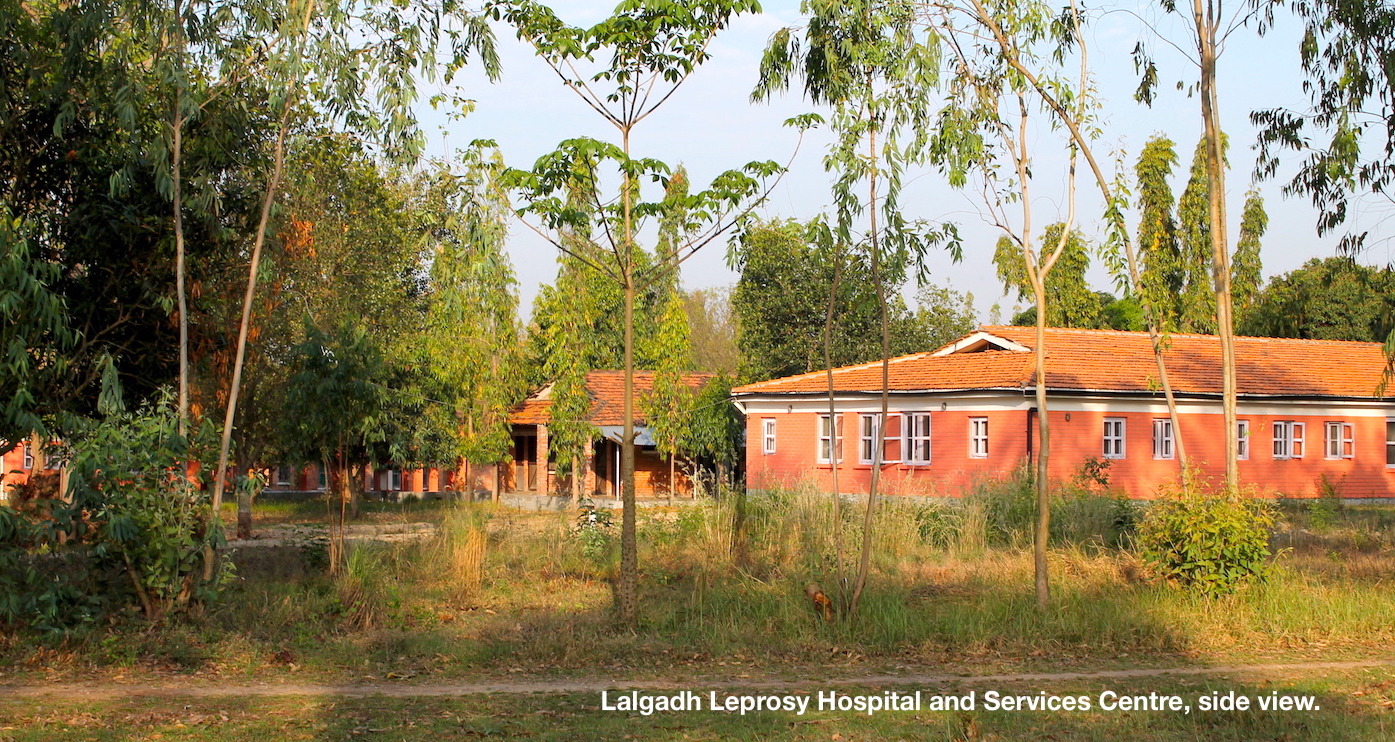 Red buildings with trees in foreground at Lalgadh Leprosy Hospital and Services Centre