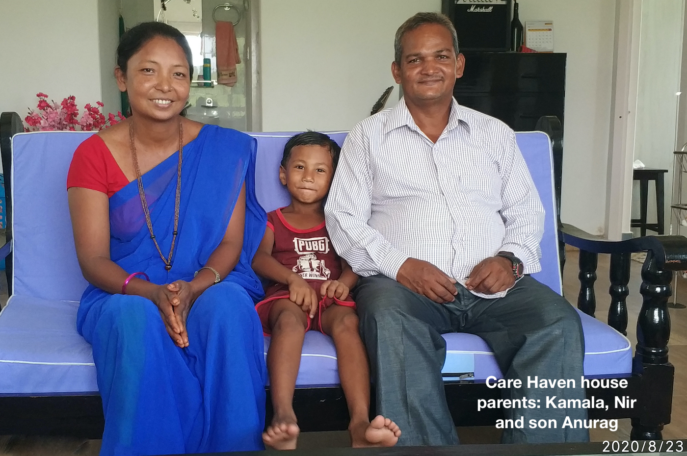 Smiling mother (L), son (m) and father (R), Kamala, Anurag and Ni, sitting on blue sofa
