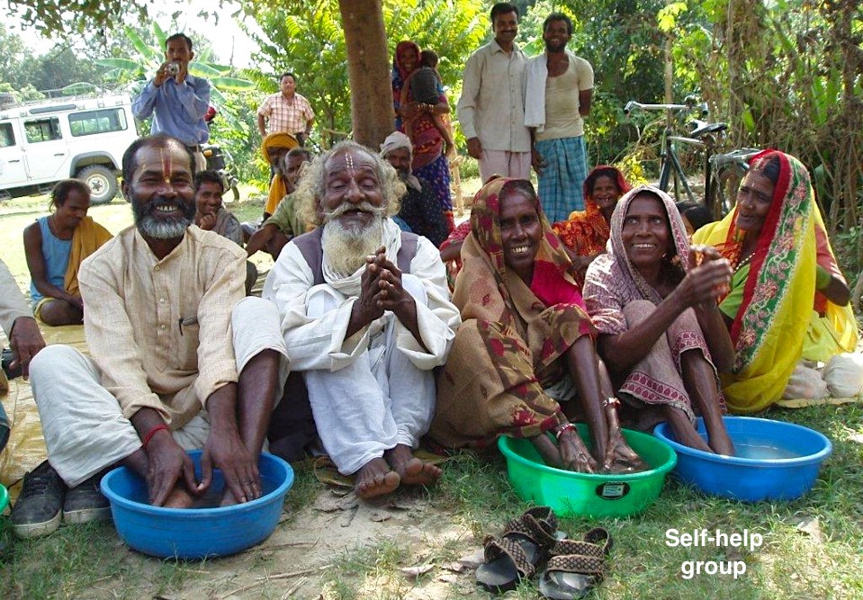 Men and women washing their feet in plastic bowls under a tree